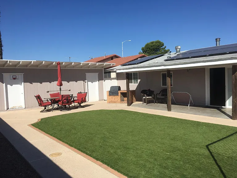 Artificial turf, large workshop, covered patio, solar roof panels, sliding glass door access.