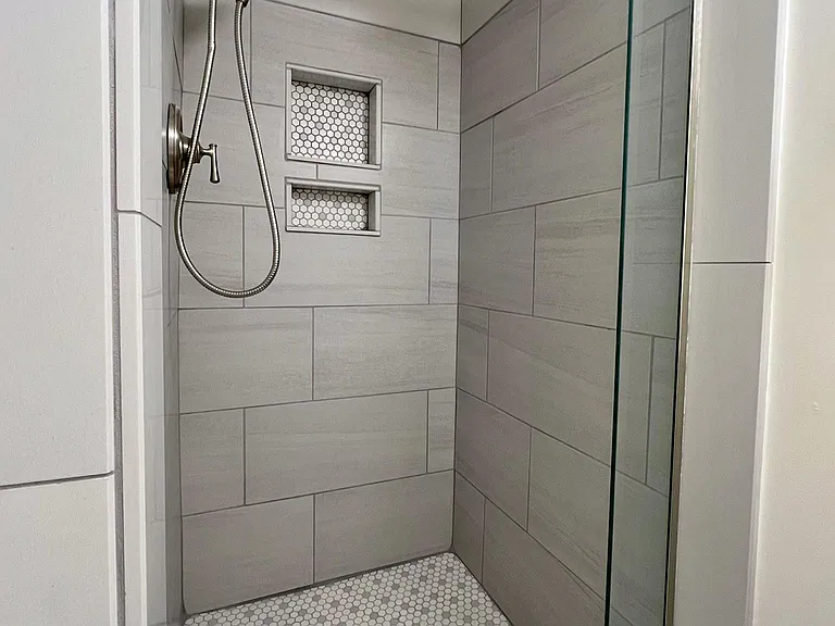 Shower with modern porcelain wall tile, classic hexagonal floor tiling, convenient inset, and magnetically-held shower head