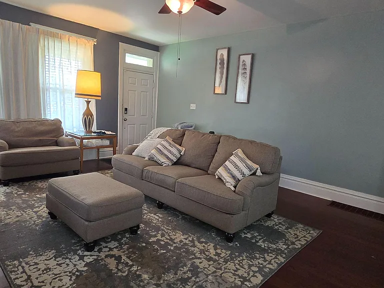 Living room with large windows, ceiling fan, and a comfortable seating layout centered on an area rug.