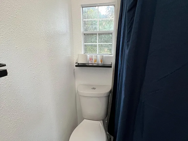 Compact bathroom featuring a tub/shower with curtain, modern toilet, and a window that provides natural ventilation.