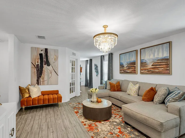 Spacious living room with a sectional seating area, stylish chandelier, and easy-care flooring with window treatments.