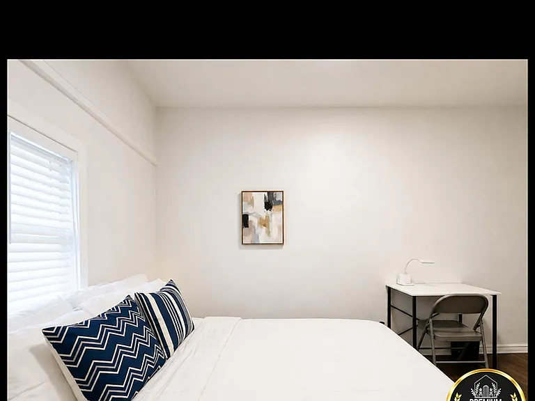 Furnished bedroom with a full bed, window blinds for light control, and a compact desk workspace for studying or WFH.