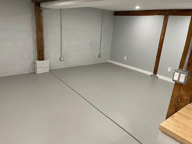 Open floor plan leads from the kitchen into the living room with cool concrete floors, walls and industrial look electrical outlets and thick wooden beams