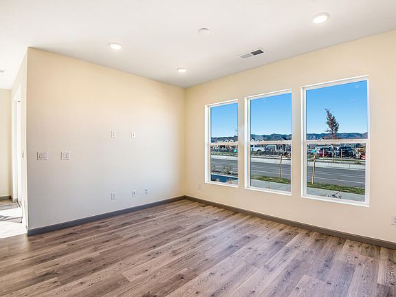 A spacious, well-lit room with large windows overlooking a street scene outside, featuring hardwood
