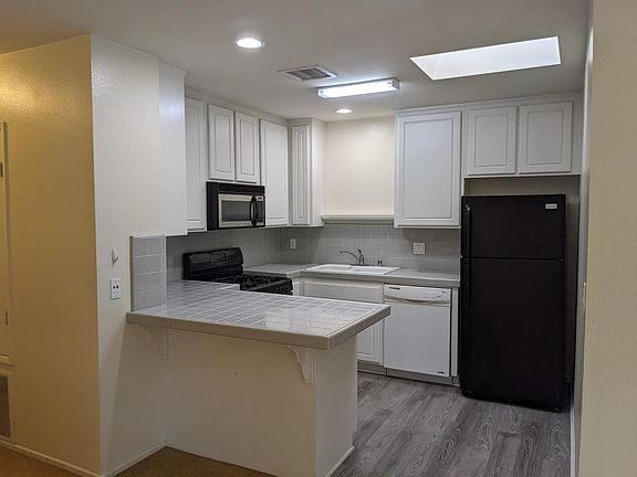 Kitchen with tile counters, gas range, dishwasher, refrigerator, microwave, and skylight.
