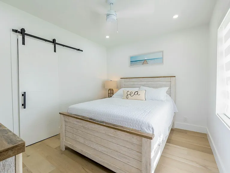 Well-appointed bedroom featuring a queen bed, ceiling fan, and a barn-style door, with window shades for privacy.