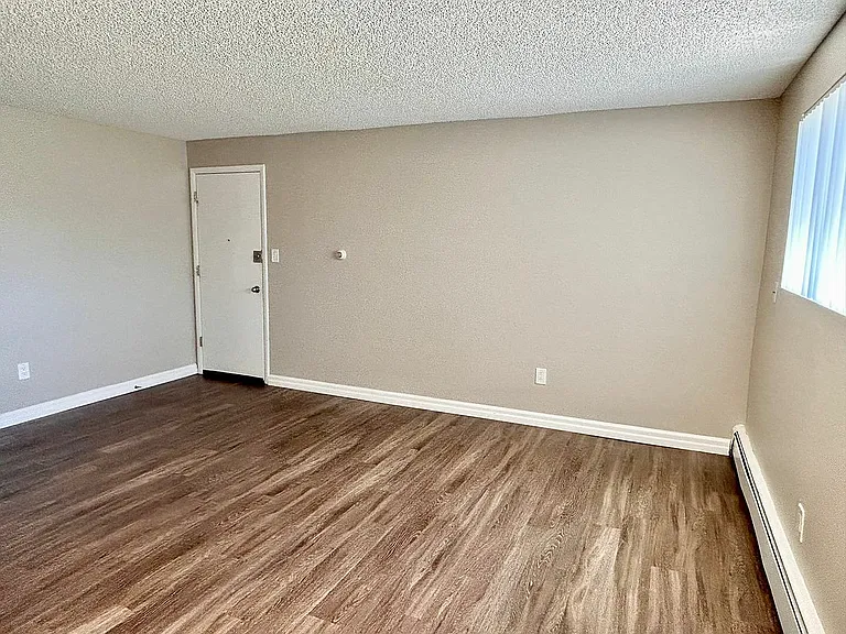 Inviting empty room with sleek hardwood floors, cream walls, and ample natural light from a large window, ideal for versatile decor opportunities.