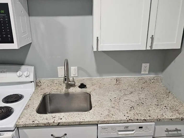 Kitchen workspace features a granite-look countertop, stainless sink, dishwasher, and ample white shaker cabinetry.