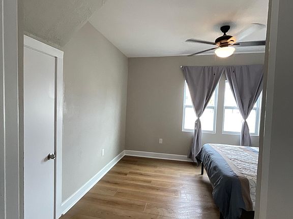 Spacious bedroom with hardwood-style floors, ceiling fan, and twin windows with curtains for comfortable natural light.
