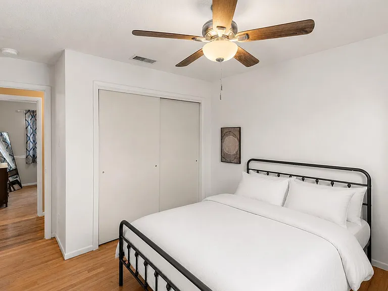 Furnished bedroom with hardwood floors, ceiling fan, and sliding-door closet plus easy access to the adjoining bath.