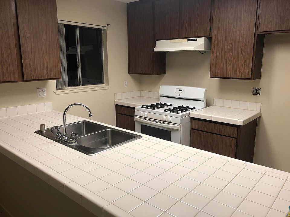 Kitchen has tile countertops, includes stove, dishwasher, and garbage disposal.
