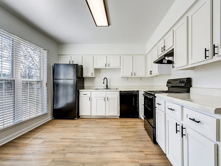 A large, open-concept kitchen with white cabinetry, black appliances, and floor to ceiling windows is shown at ReNew on Cantrell.