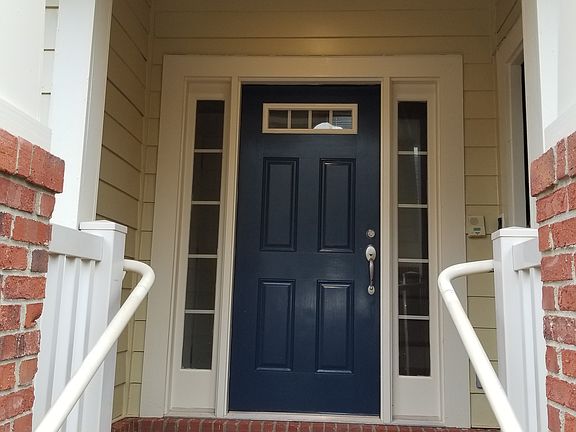 Inviting front entrance with a blue door, transom window, and white trim. Set against a brick facade with matching steps and railings for classic curb appeal.