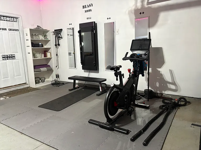 Private home fitness studio featuring a Tonal smart gym system, Bowflex Velocore bike, kettlebells, and additional workout equipment for a true wellness-focused lifestyle at home.