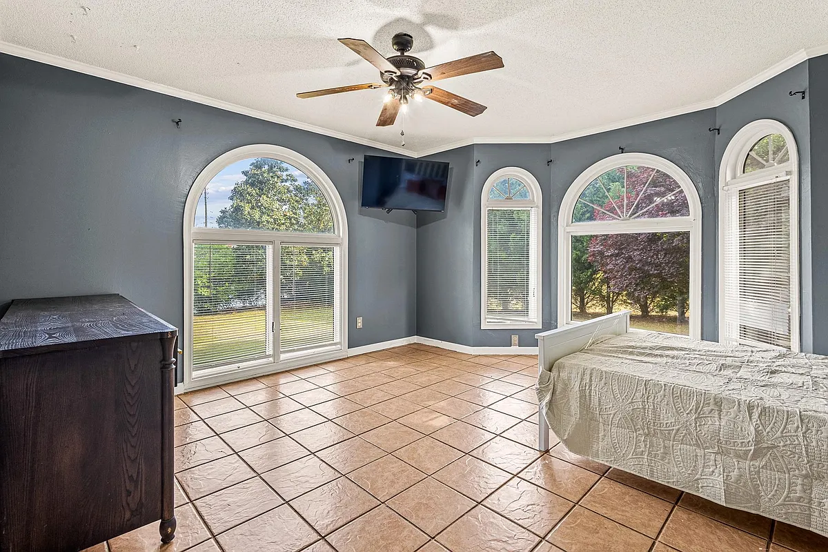 Spacious bedroom with arched windows, tile flooring, ceiling fan, and wall-mounted TV for comfortable everyday living. - Jonesboro Rd