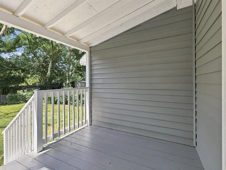 Covered porch with white painted railing, gray siding, and exposed white ceiling joists