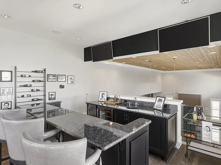 Upstairs mini bar conveniently located just steps from the rooftop patio and game room_perfect for mixing a drink before heading out. Two TVs located above the bar and a wine bottle shelf.