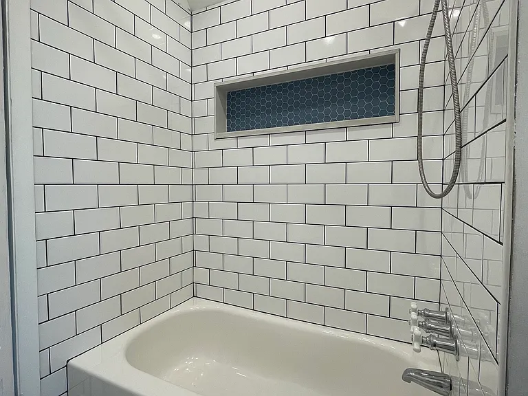 Full bathroom featuring a tub and shower combination, classic white subway tile, and a built-in niche with blue accent tile for added style and convenience.