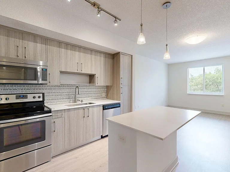 Apartment kitchen with stainless steel appliances, light counters, and wood style floor.