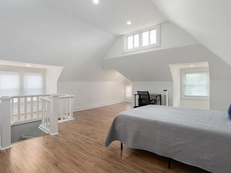 Spacious loft-style bedroom with vaulted ceilings, hardwood floors, and multiple windows plus a small work area.