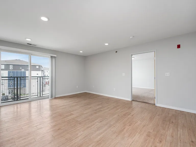 Bright and spacious living room with modern wooden flooring, large windows offering plenty of natural light and a view of the surrounding area, leading to a cozy adjacent room. Bright and spacious living room with modern wooden flooring, large windows off