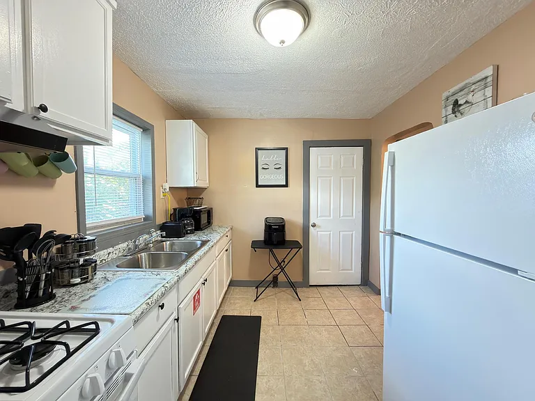 Galley kitchen with ample cabinetry, double-basin sink, and full-size refrigerator plus a window over the counter.
