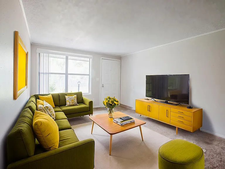 Chic living room with vibrant green sofa, stylish yellow accents, and a sleek modern coffee table under natural light from a large window.