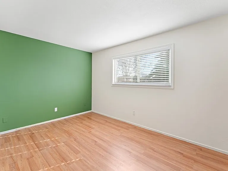 Bedroom #2 freshly painted with a striking forest green accent wall, new blinds, updated flooring, and a built-in closet.