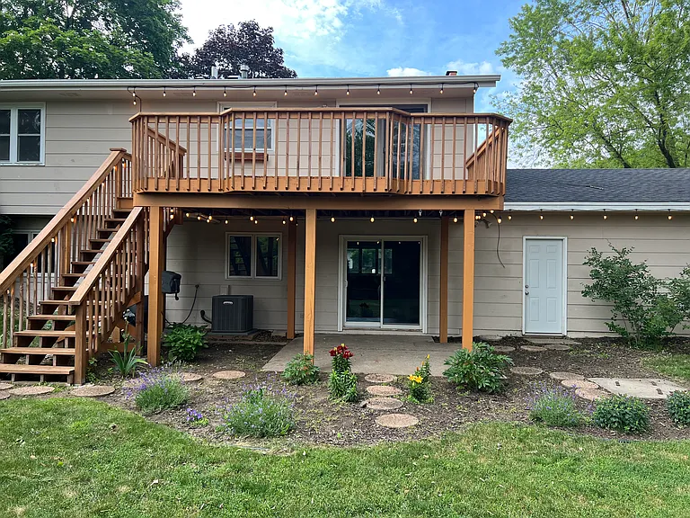 Fully fenced backyard with firepit, raised garden bed, perennial flowers, string lights, and large deck.
