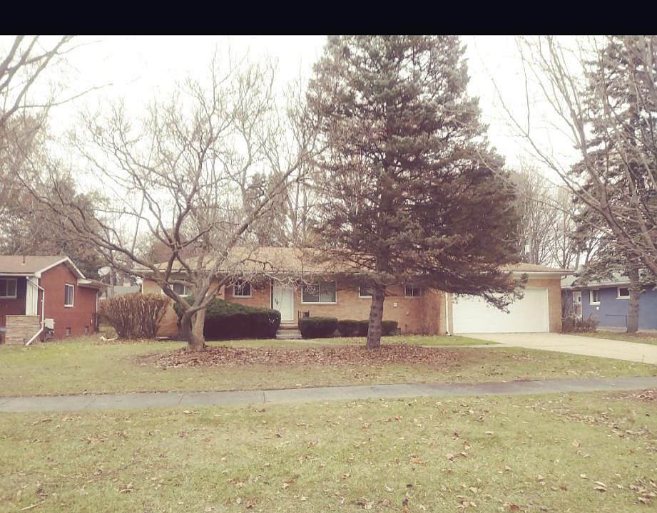 Beautiful brick ranch set back on a large green front lawn with flowering trees and evergreens .