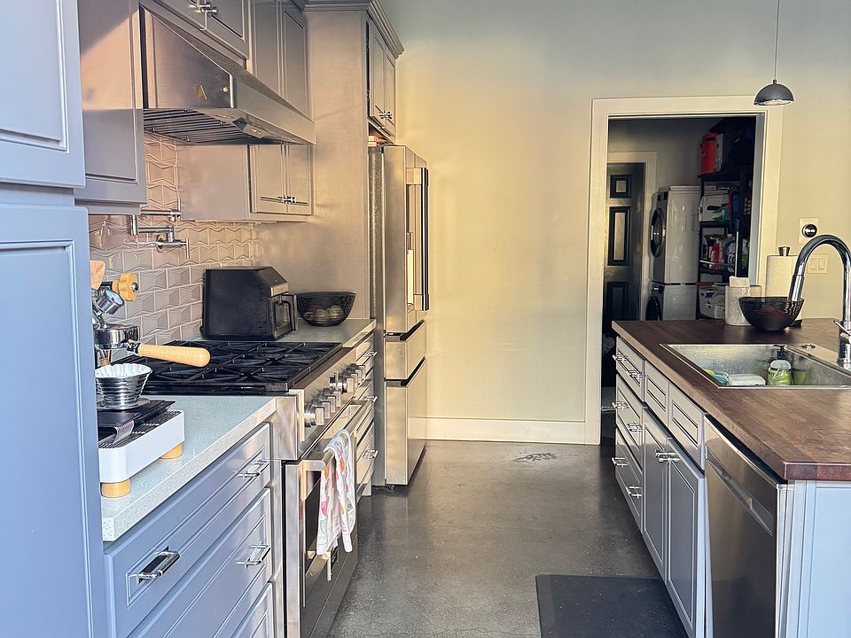 Kitchen with wide aisleway. Stainless appliances, 36" gas range/oven, powerful exhaust fan, tile backsplash, pot filler, quartz countertops. Center island has dishwasher, deep basin sink, walnut butcher block, and room for seating.