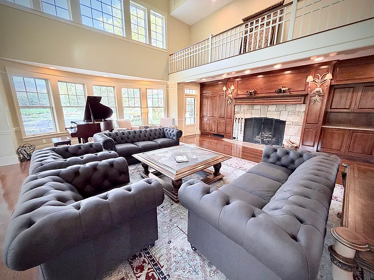 View of the richly decorated great room with seating for up to seventeen, a massive stone fireplace, and a grand piano.