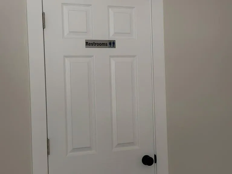 Interior door leading to a shared restroom area with neutral walls and simple trim detail.