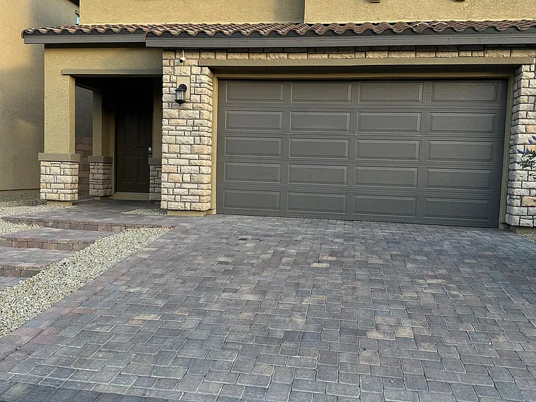 Two-story stucco home with stone accents, a covered entry, and a wide paver driveway leading to a two-car garage.