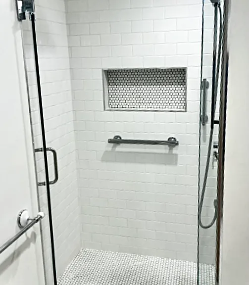 Luxury shower with glass doors, curbless entry, ceiling mounted waterfall showerhead, plus shower wand, and shampoo niche.