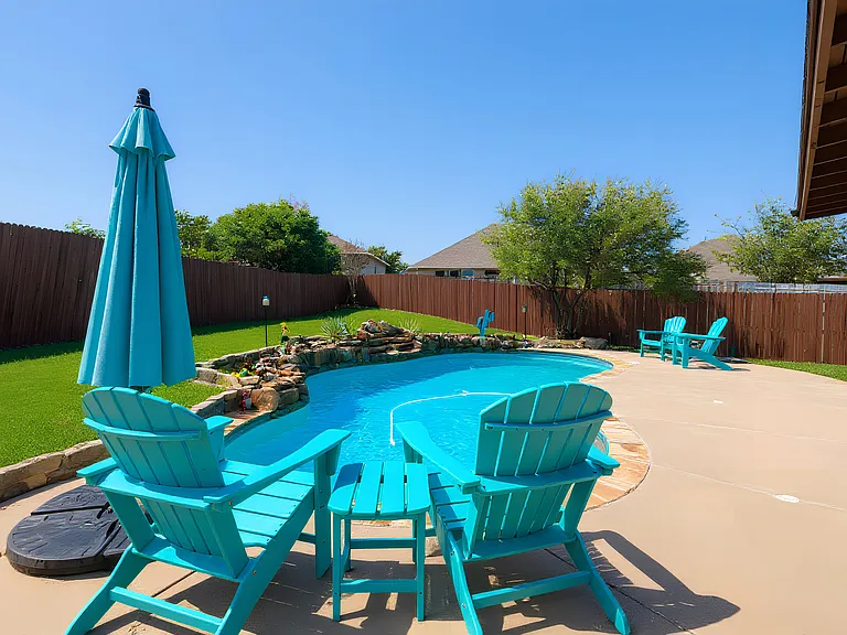 Relax in the private backyard with a sparkling pool, waterfall feature, and Adirondack seating. A perfect spot for sunny lounging and outdoor enjoyment.