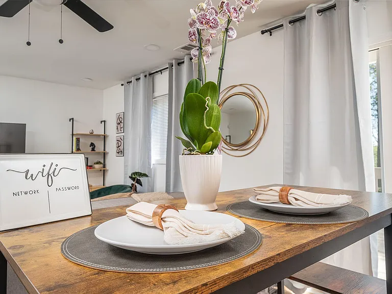Dining area with a bar-height table setting, open sightlines to the living space, and window light with curtains.