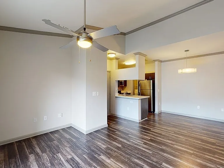 Apartment kitchen with stainless steel appliances, dining and living room with wood-style flooring.