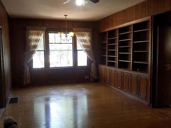 A large window, shelves, and wood paneling circumscribe the library, and this is one end of the room