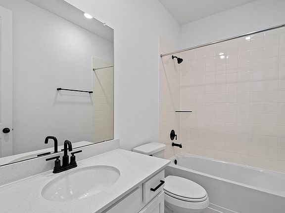 The secondary bath features tile flooring, white cabinetry and light countertops and a shower tub co
