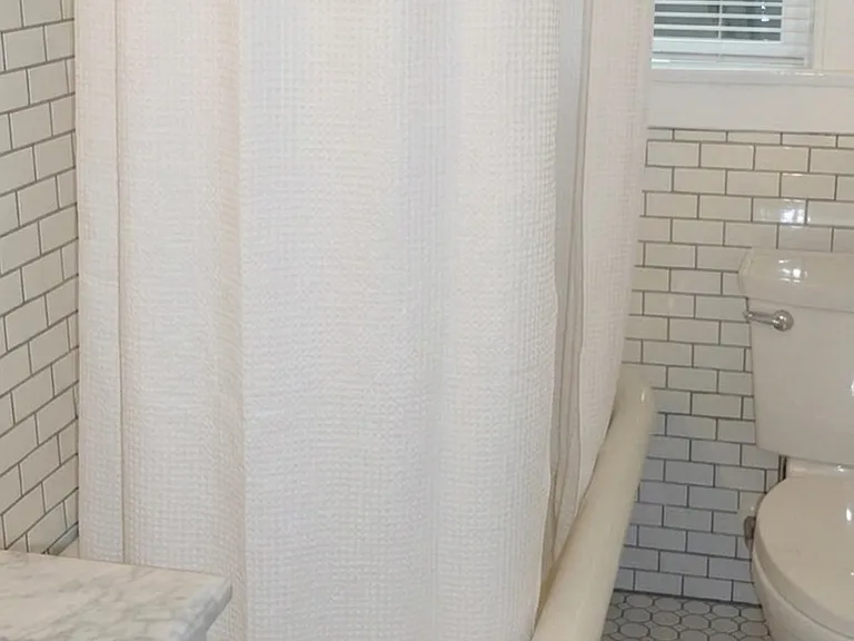 Subway tiled bathroom with clawfoot tub and updated vintage-style fixtures. (Shower curtain is virtually staged)