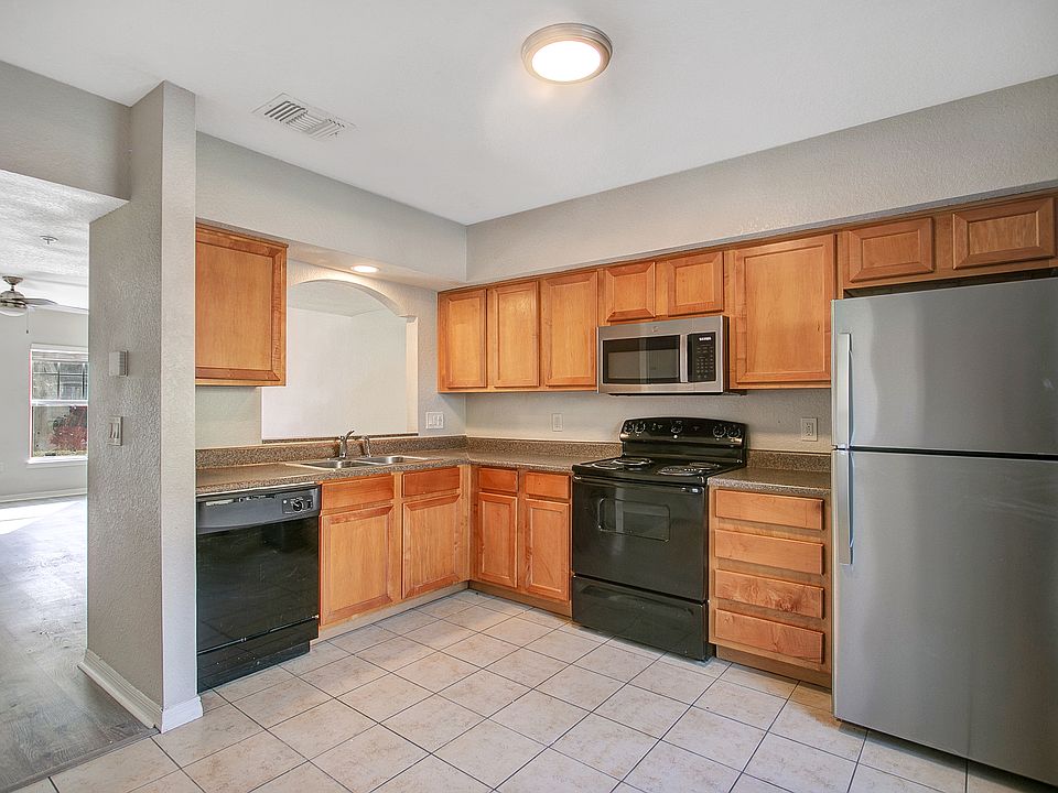 apartment kitchen featuring wooden cabinets, tile flooring, dishwasher, range, microwave, and stainless steel refrigerator