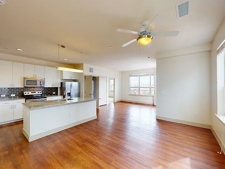 Apartment kitchen with stainless steel appliances, dining and living room with wood-style flooring.