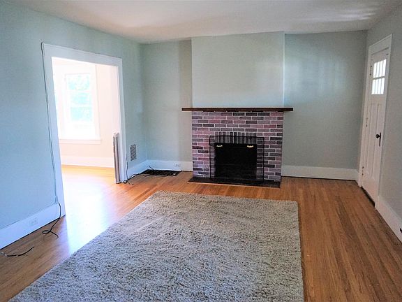Another look at the living room we see the attractive fireplace hearth & mantle making a wonderful focal point for the room. To our right is a doorway stepping out to a fantastic sleeper porch.