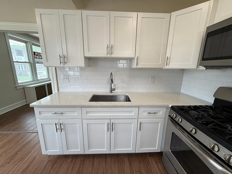 Modern sink area with updated countertop, white cabinets, and tile backsplash.
