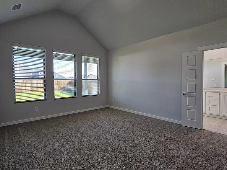 Relax in the spacious primary suite, featuring neutral tones and large windows overlooking the backyard