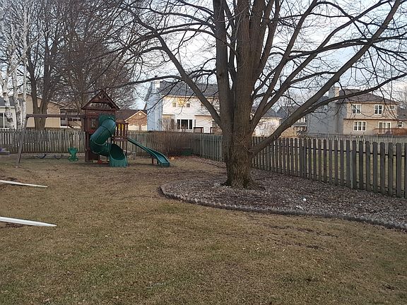 Landscaped backyard with mature trees and children's playset