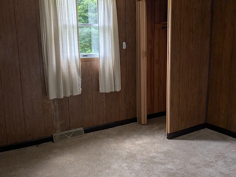 Small den, tan carpet, single window.