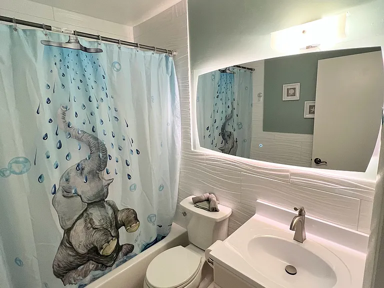 Refreshed guest bath with new tile, tall toilet, sink, mirror, and shower fixtures