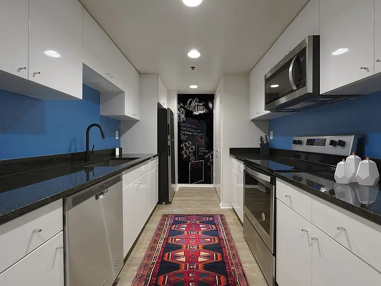 Renovated Package I kitchen with black granite countertops, stainless steel appliances, white cabinetry, blue painted backsplash, and hard surface flooring